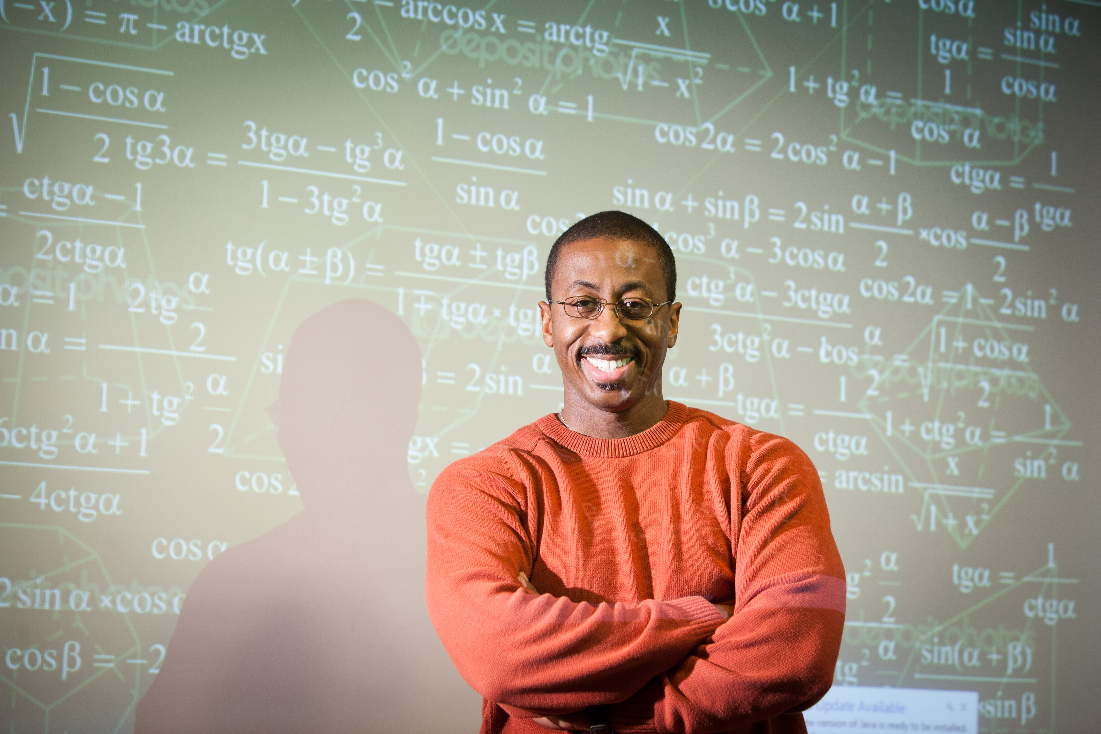 Photo showing a Professor standing in front of a chalk board and facing his students.