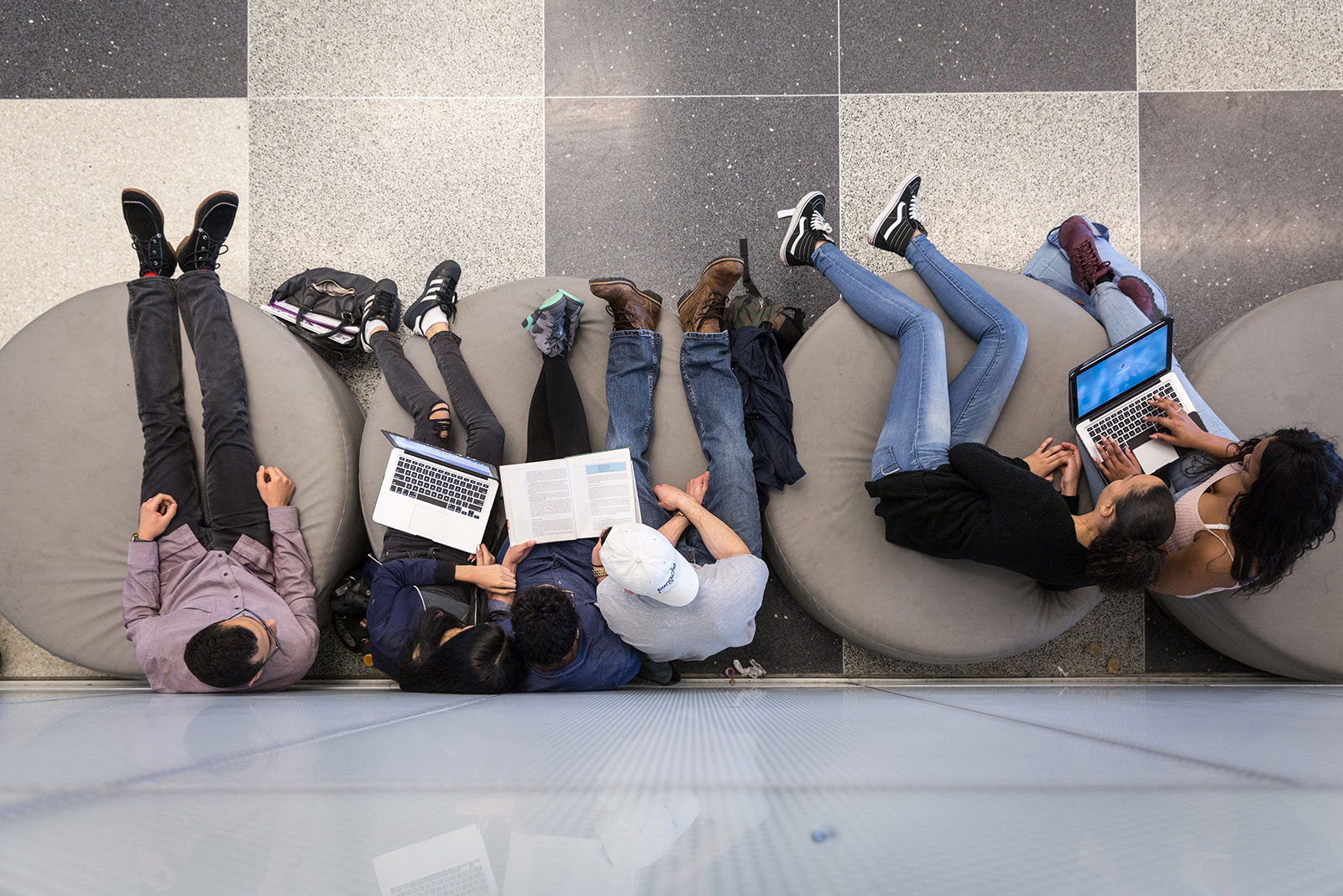 Five students sitting and two of them are on laptops.