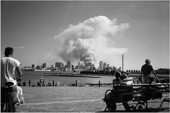 Black and White Photo where people staring are at Manhattan skyline with smoke in the skiy