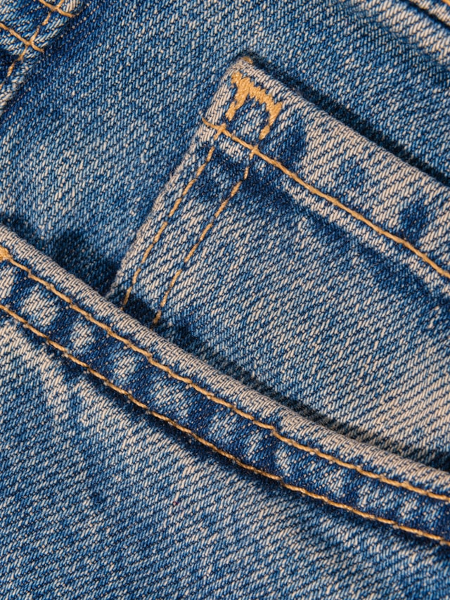 Close-up of blue denim jeans showing a front pocket with visible stitching and seam details