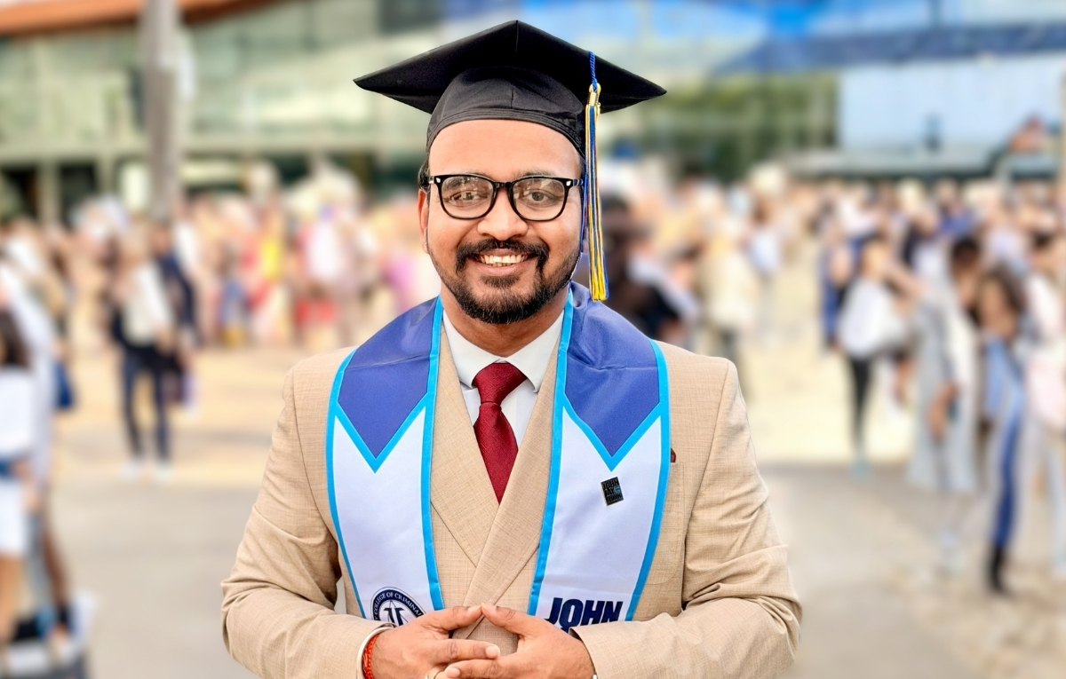 Avijit Roy wears his graduation cap and stole, a tan suit, white shirt and red tie, and smiles at the camera.