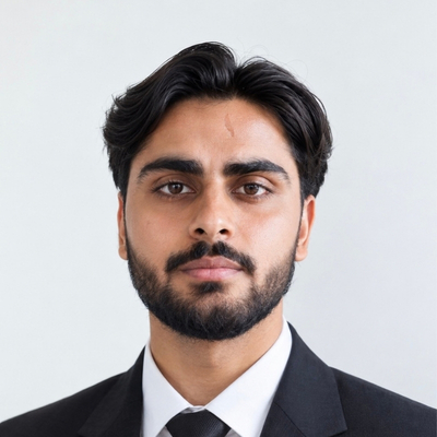 Student Ali Hassan is wearing a dark suit, white shirt and dark tie. He is facing the camera and standing against a light grey background.