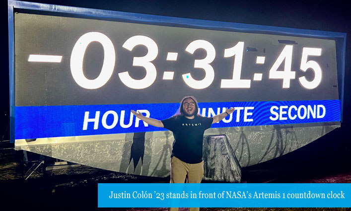 Justin Colón ’23 stands in front of NASA’s Artemis I countdown clock 