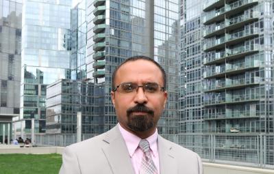 Professor Jason D. Rivera wearing a gray suit and pink shirt on the John Jay College Jaywalk