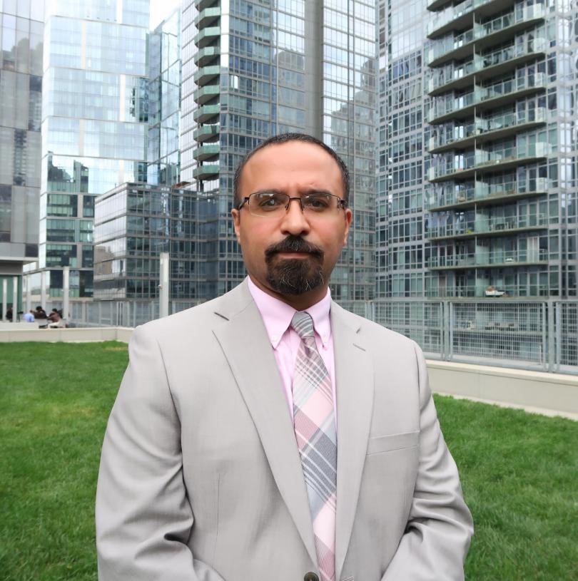 Professor Jason D. Rivera wearing a gray suit and pink shirt on the John Jay College Jaywalk